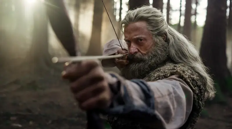 Fotograma de la película La muerte de Robin Hood con un primer plano intenso de Hugh Jackman apuntando con su arco y flecha directamente en medio del bosque.