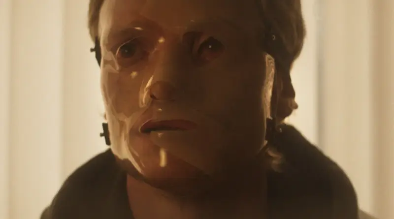 Hombre con el rostro cubierto por una máscara médica de plástico transparente sujeta con correas en Clayface.