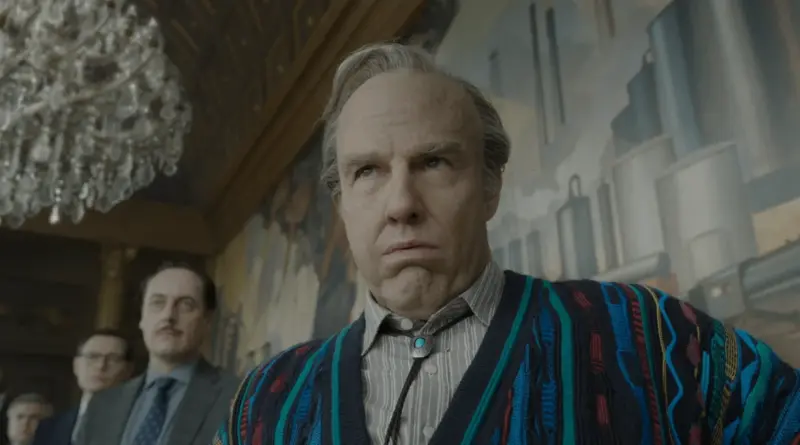 Personaje de la película Digger. Un hombre mayor con calvicie y una chaqueta de punto colorida mira hacia arriba con gesto de desconcierto.