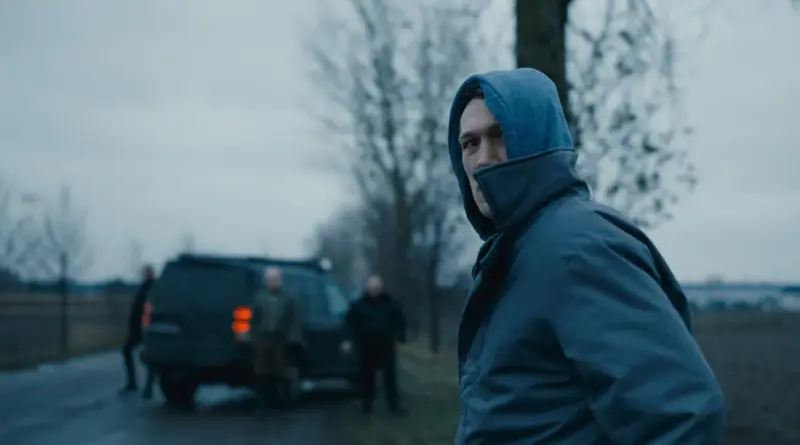 Un joven con capucha azul mira tenso hacia atrás en un paisaje nublado en la película 'Kingdom' ('Królestwo').