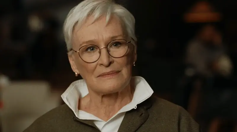 Primer plano de la actriz Glenn Close en una escena de La bola negra, luciendo cabello blanco corto y gafas doradas con una expresión calmada.