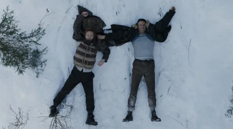 Toma aérea de Branagh y Reynolds tendidos sobre un suelo nevado en la película Mayday.