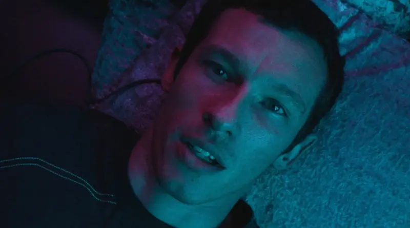 Fotograma de la serie Neuromante con un plano cenital de Callum Turner iluminado por luces neón en tonos cian y magenta.