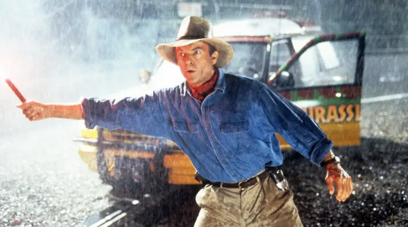 Sam Neill como el Dr. Alan Grant en la película Jurassic Park, de pie bajo la lluvia sosteniendo una bengala roja encendida.