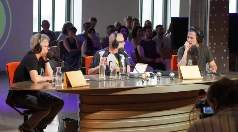 Tres hombres sentados en una mesa de podcast curva durante la transmisión final de la temporada 12 de "Todopoderosos".