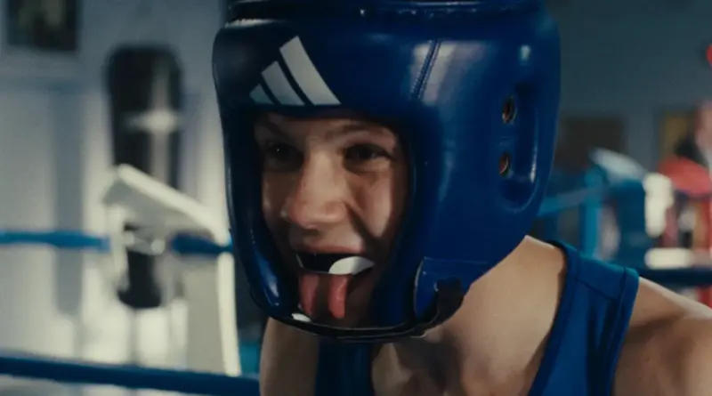 Primer plano del joven protagonista de Wild Foxes con casco de boxeo sacando la lengua en el gimnasio.