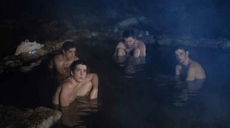 Cuatro chicos bañándose de noche en unas termas naturales humeantes en una escena nocturna de Anoche conquisté Tebas.