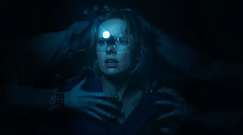 Escena oscura de Insidious: Fuera del Más Allá donde la protagonista, iluminada solo por una linterna de cabeza, es agarrada desde las sombras por múltiples pares de manos espectrales.