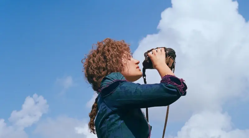 Una mujer joven de cabello rizado bebiendo de una cantimplora rústica bajo un cielo azul brillante en La apuesta de Buffalo Bill.