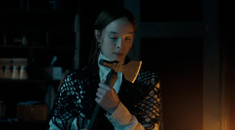Escena oscura de Monstruo: La historia de Lizzie Borden en la que la protagonista sostiene un hacha muy cerca de su pecho, mirándola con devoción.
