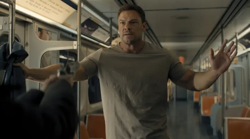 Jack Reacher con las manos en alto frente a un agresor que le apunta con una pistola en el vagón de un metro en la temporada 4 de Reacher.