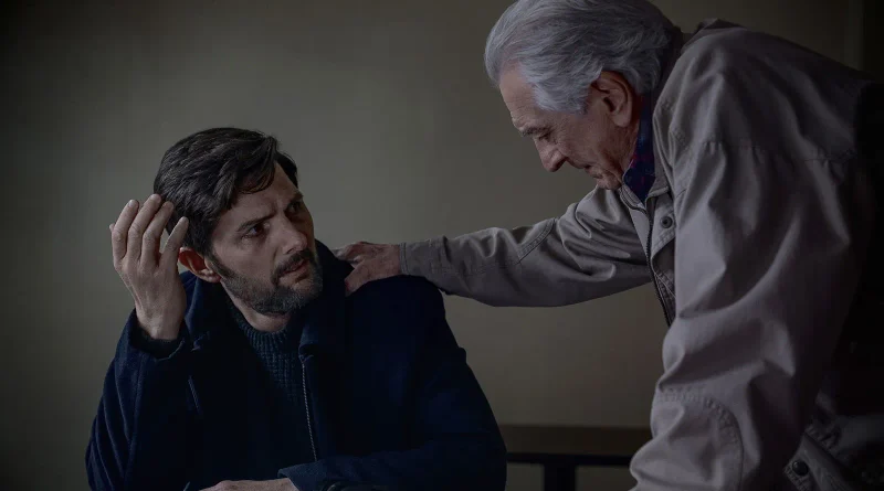 Fotograma de la película 'Susurran tu nombre' (The Whisper Man) en el que Robert De Niro apoya su mano sobre el hombro de un abrumado Adam Scott en un ambiente lúgubre.