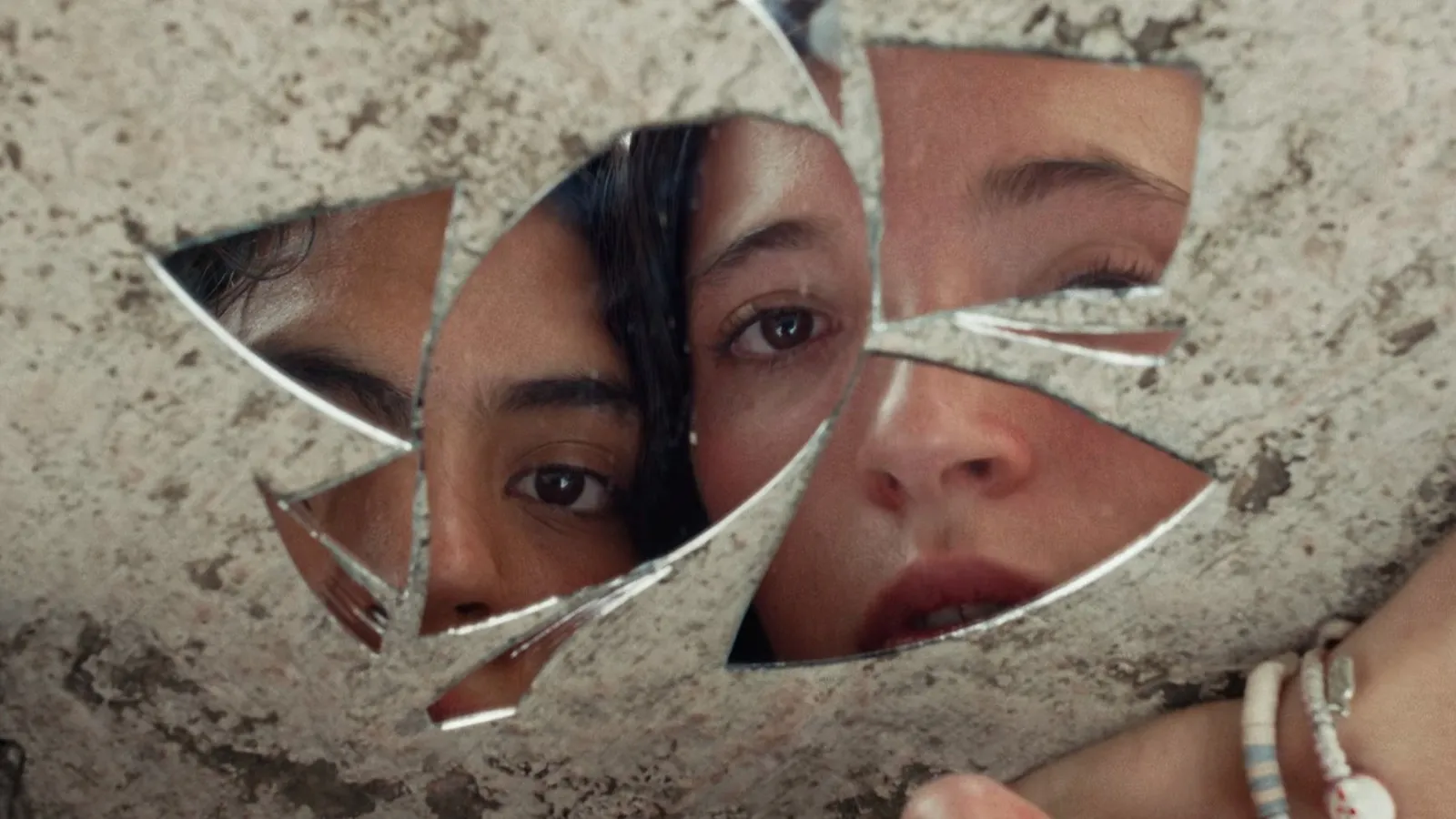 Los rostros fragmentados de las dos protagonistas de Chicas tristes reflejados a través de los pedazos de un espejo roto apoyado en el suelo.