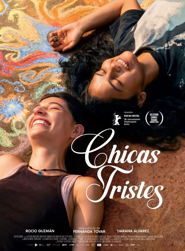 Póster oficial de la película Chicas tristes con las dos jóvenes protagonistas sonriendo y tumbadas sobre un suelo pintado de colores.