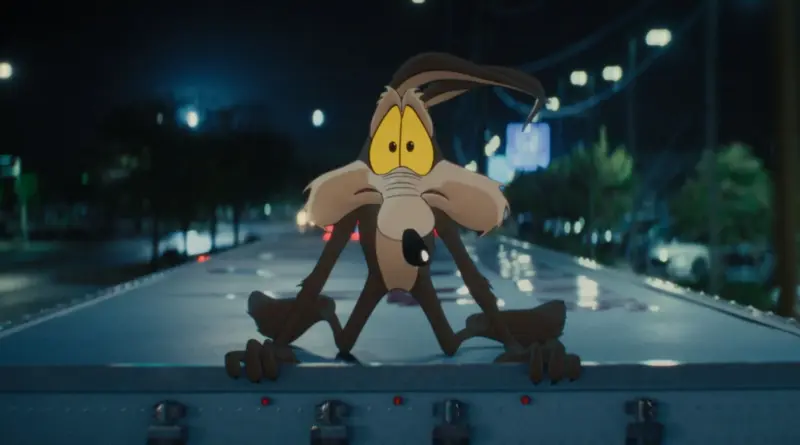 Fotograma nocturno de la película Coyote vs. ACME con Wile E. Coyote asomado sobre un camión en marcha.