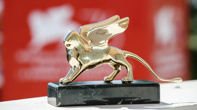 Estatuilla del León de Oro del Festival de Venecia, de acabado dorado brillante y alas extendidas, sobre una base de mármol negro, con un fondo rojo desenfocado.