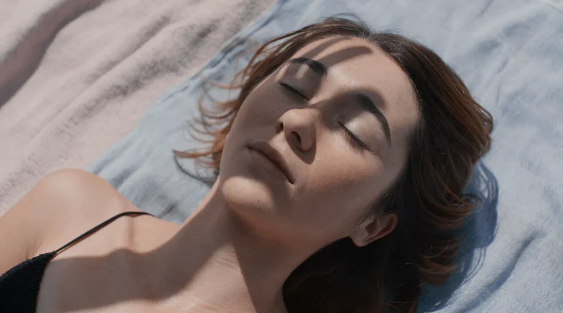 Primer plano de una joven recostada con los ojos cerrados bajo la luz del sol en la película Forastera.