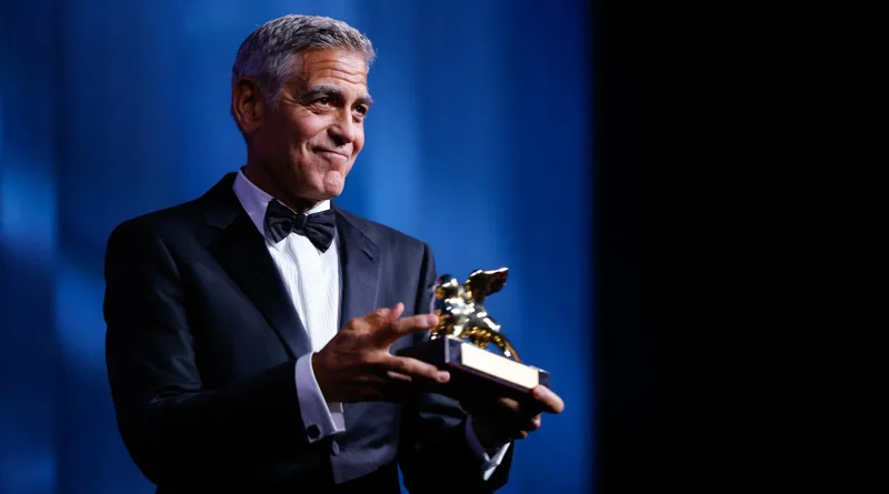 George Clooney sujeta emocionado su León de Oro honorífico frente a un fondo azul oscuro.