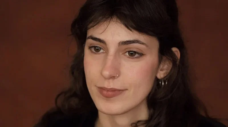 Primer plano de la cineasta Anna Llargués mirando con expresión tranquila hacia un lado, sobre un fondo liso de tono marrón cálido.