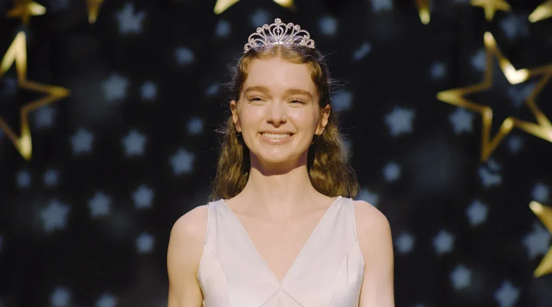Summer H. Howell como Carrie sonriendo felizmente en el baile de graduación, luciendo una tiara y un vestido blanco frente a un fondo de estrellas.