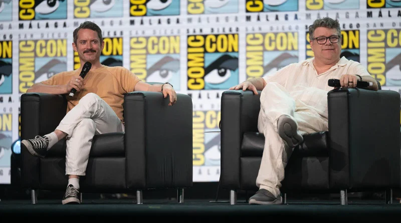 Los actores Elijah Wood y Sean Astin posando relajados y sonrientes mientras están sentados en los sillones negros del escenario.