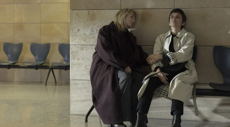 Emma Suárez y Elena Anaya sentadas juntas y cogidas de la mano con expresión de profundo agotamiento en una sala de espera en Hermanas.