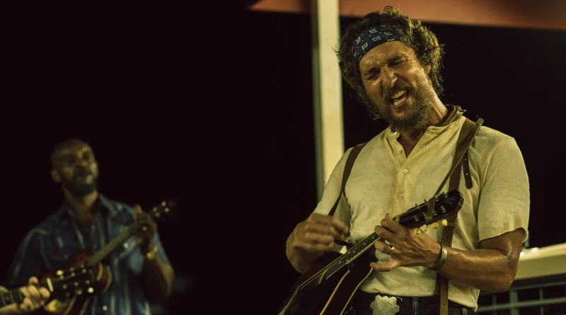 Matthew McConaughey tocando la mandolina y cantando con pasión durante una actuación musical nocturna en Los rivales de Amziah King.
