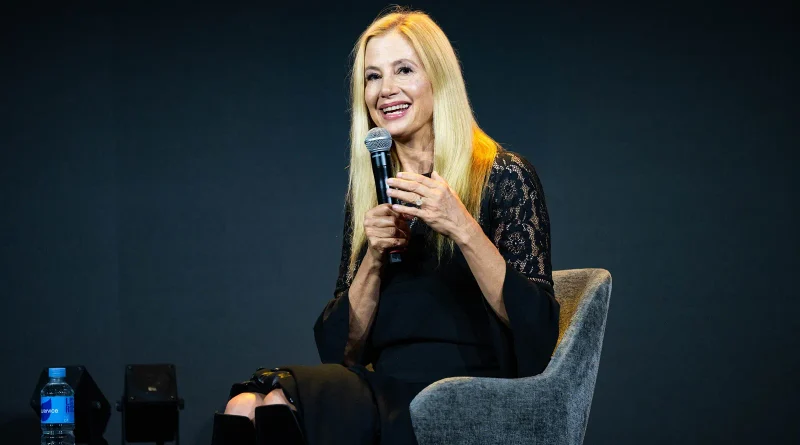 Primer plano de Mira Sorvino sonriendo abiertamente mientras habla por un micrófono durante su intervención en la convención.