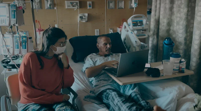 Sergio Peris-Mencheta en su cama de hospital trabajando con un ordenador portátil, acompañado por una mujer con mascarilla, en una escena del documental SerYo.